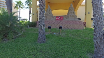 A sign for 'Ramada South Padre Island' with a brick wall and palm trees in the foreground.