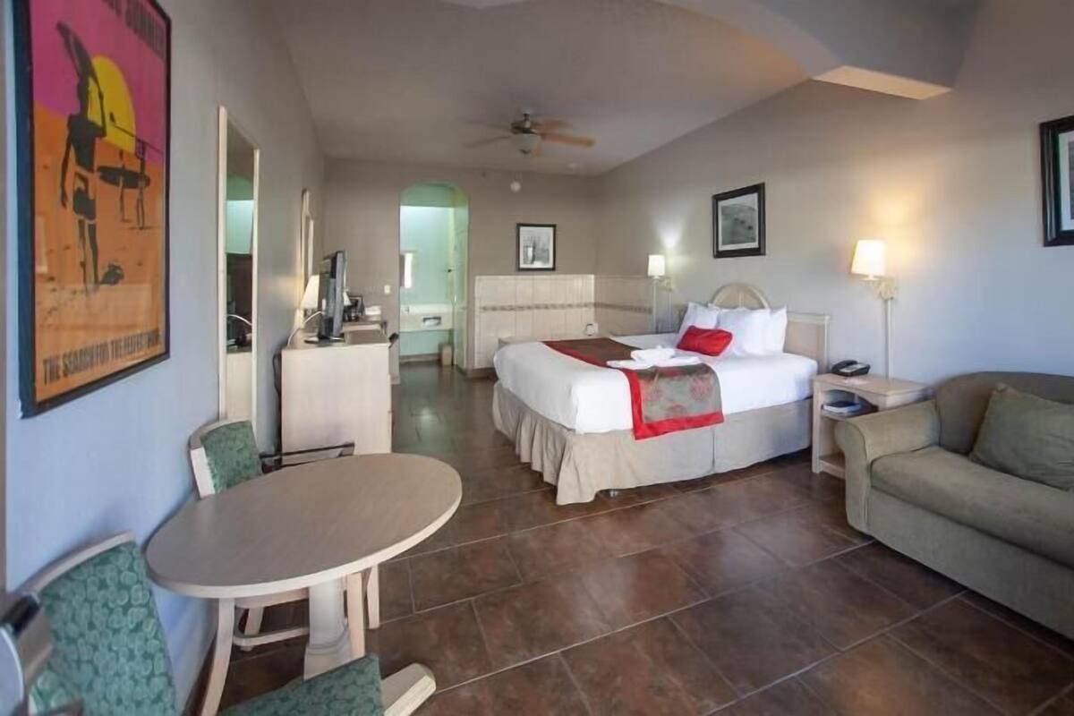 A hotel room with a bed, a sofa, a desk, a chair, and a dining table.