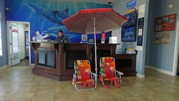 A reception desk with a large poster of a whale, two beach chairs, and a red umbrella.