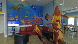 A lobby with a large aquarium mural, a red sofa, black chairs, and a dining area with wooden tables and chairs. - Ramada by Wyndham & Suites South Padre Island At the Beach (South Padre Island)