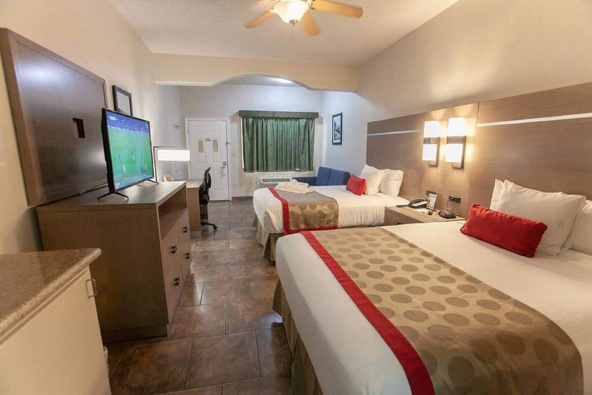 A hotel room with a TV, two beds, a desk, and a chair.