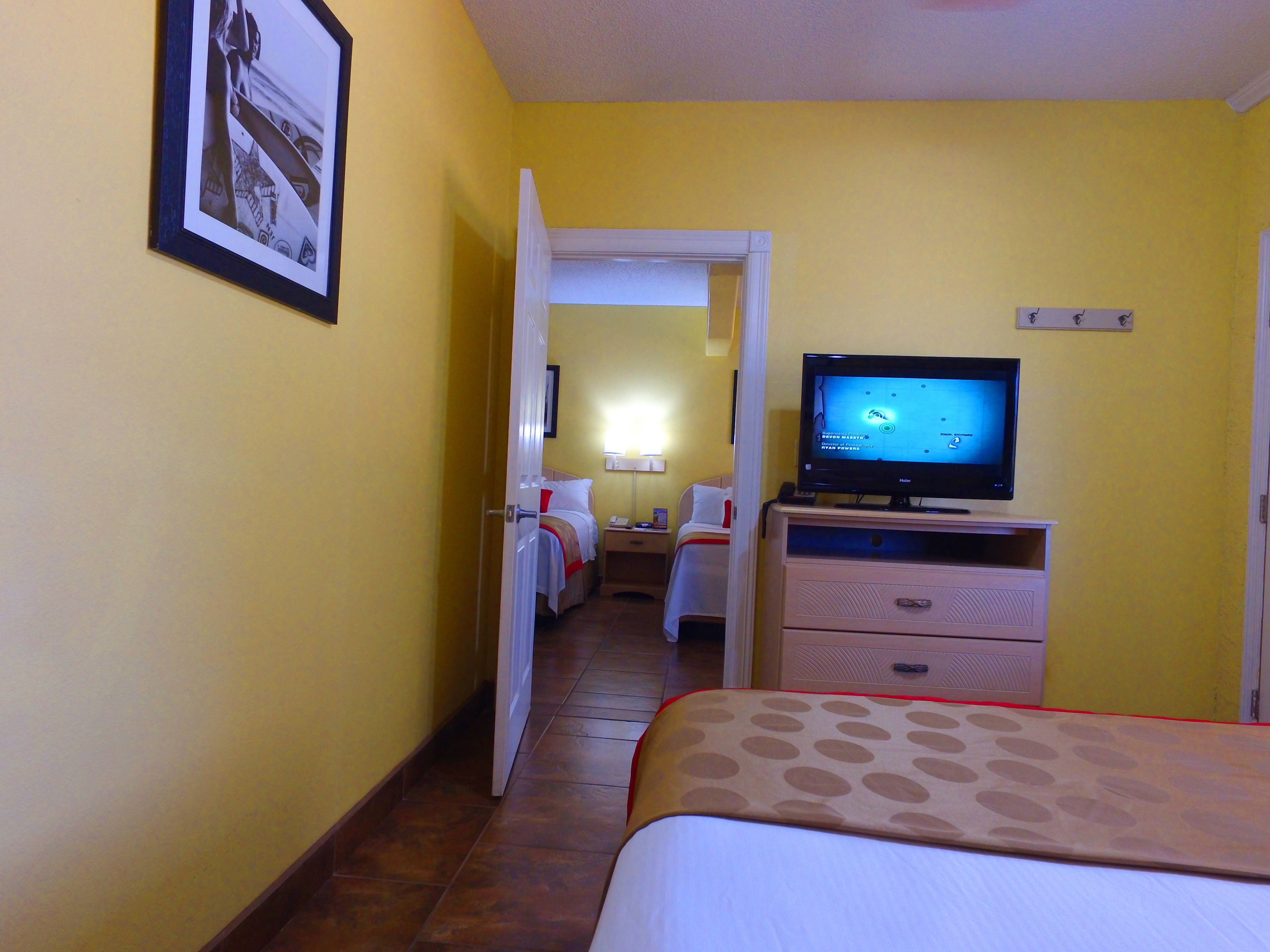 A hotel room with a bed, a television, a dresser, and a door leading to another room.