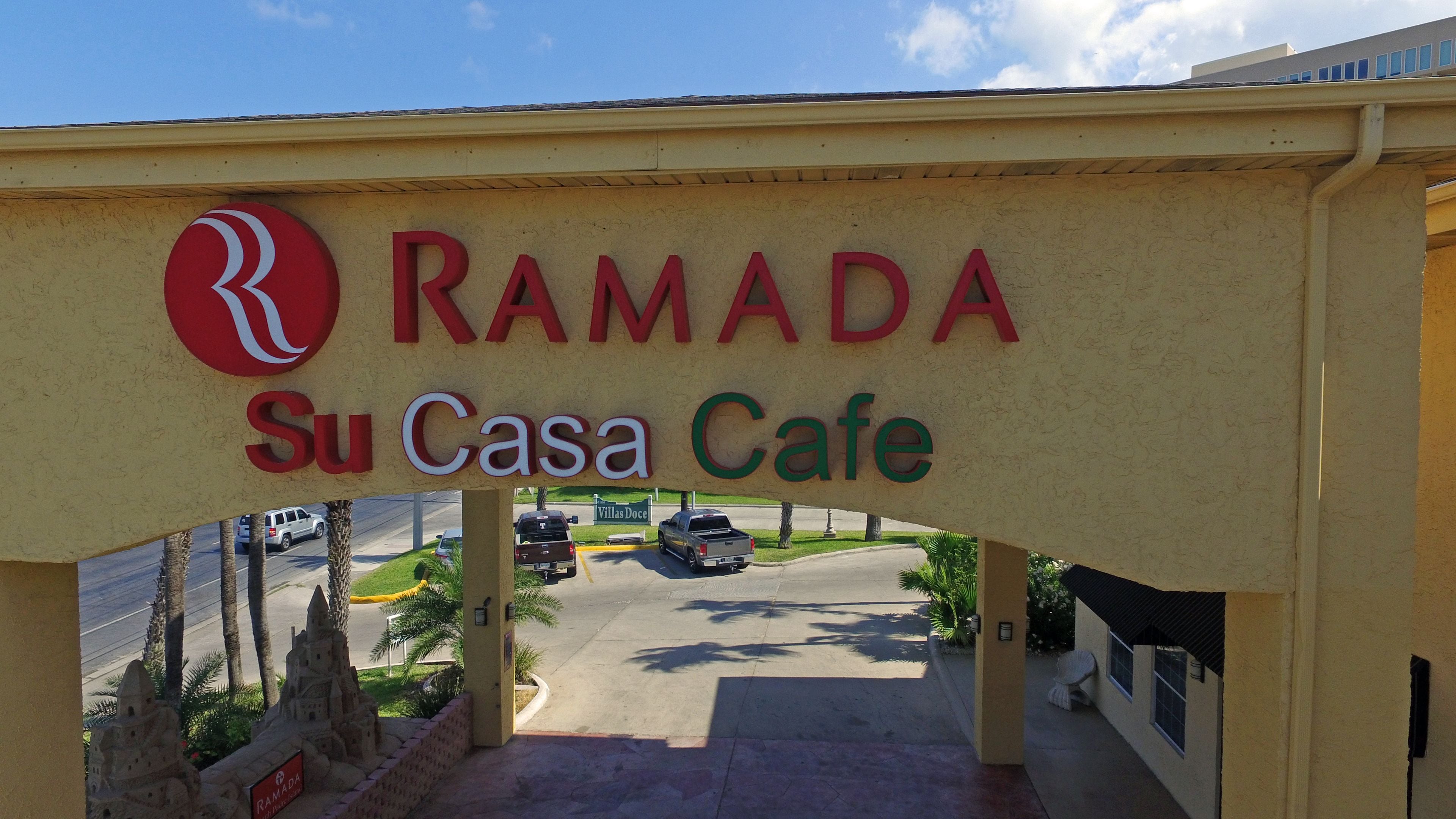 A sign for Ramada Su Casa Cafe with a clear view of the parking area and a small palm tree model.