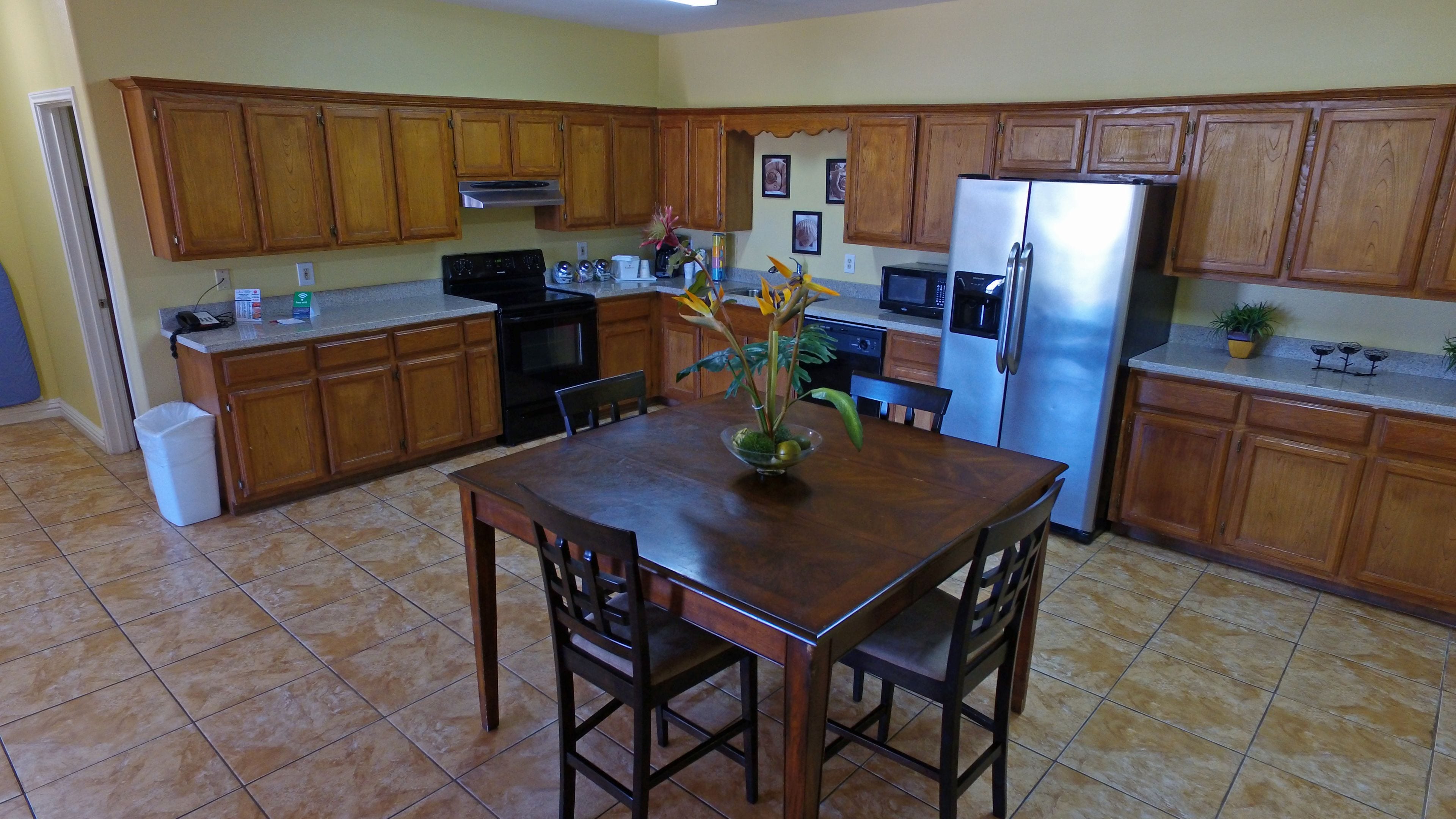 Una cocina con armarios de madera, un refrigerador de acero inoxidable, un microondas y una mesa de comedor con sillas.