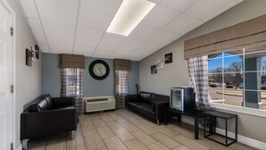 Un salon avec un canapé, un téléviseur, une horloge et une fenêtre avec des rideaux.
