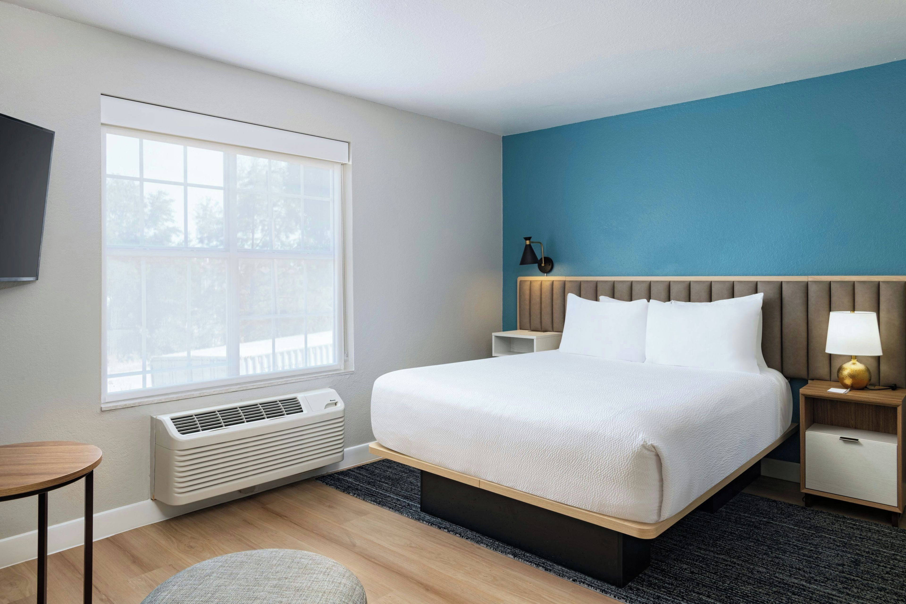 A hotel room with a large bed, bedside tables, a lamp, and a window with blinds.