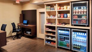 A small office area with a desk, computer, and chairs, and two refrigerated beverage dispensers stocked with various drinks. - TownePlace Suites by Marriott Dallas Las Colinas (Irving)
