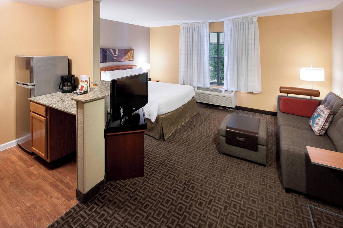 A hotel room with a kitchenette, a bed, a sofa, and a TV.
