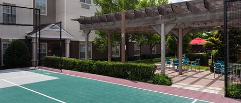 An outdoor tennis court with a wooden pergola and seating area.