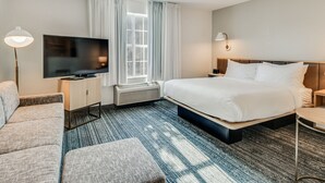 A hotel room with a bed, a TV, a sofa, a desk, and a window with curtains.
