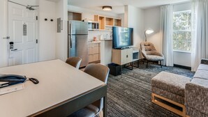 A compact hotel room with a kitchenette, a flat-screen TV, a sofa, and a dining table.