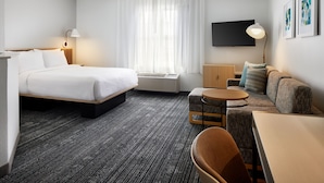 A hotel room with a bed, a sofa, a small table, a TV, and a window with curtains.