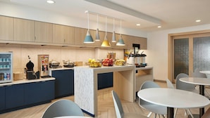 A modern kitchen with a marble island, pendant lights, and a seating area with round tables and chairs.