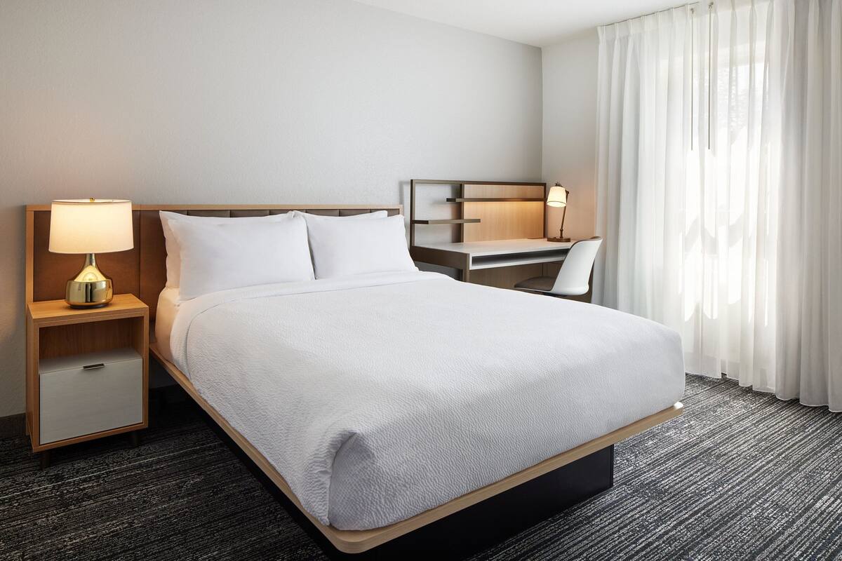 Hotellihuone, jossa on sänky, työpöytä, tuoli, yöpöytä ja lamppu.