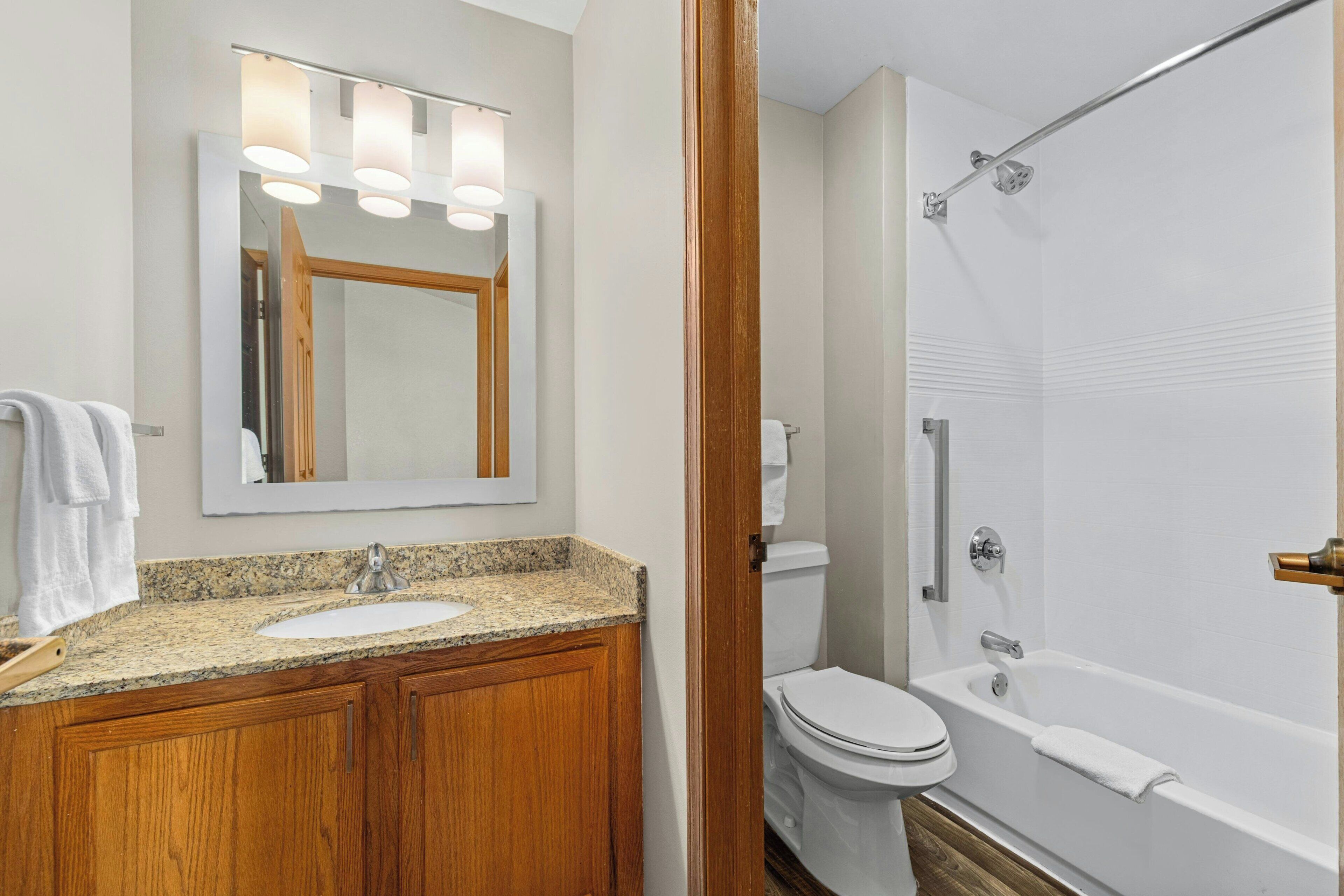 Une salle de bain avec un meuble-lavabo en bois, un évier, un miroir, des toilettes et une baignoire.