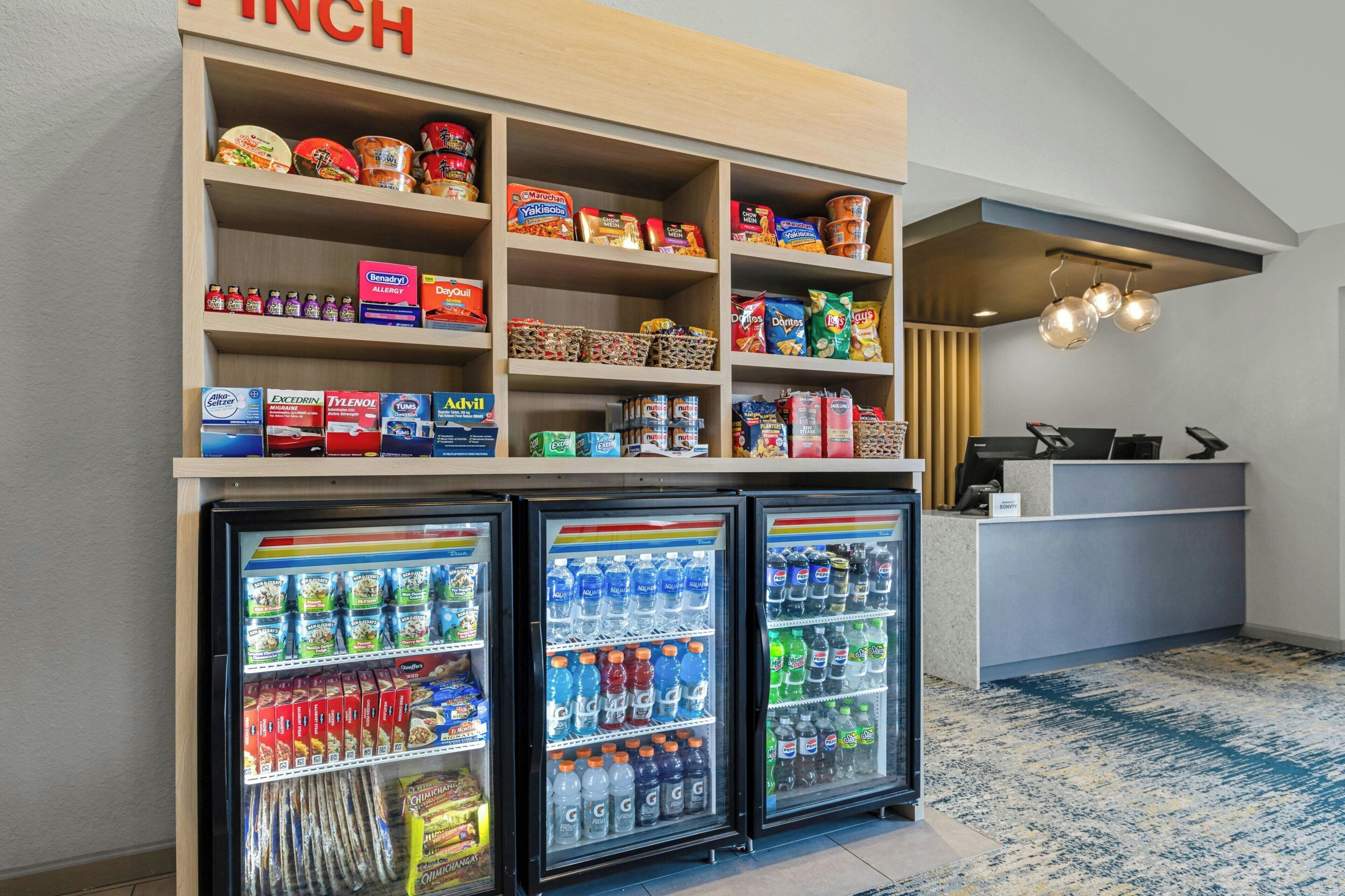 Un espace d’accueil d’hôtel comprenant un présentoir à collations, un comptoir et trois réfrigérateurs à boissons.