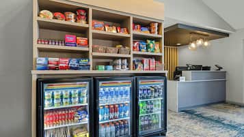 Un espace d’accueil d’hôtel comprenant un présentoir à collations, un comptoir et trois réfrigérateurs à boissons.