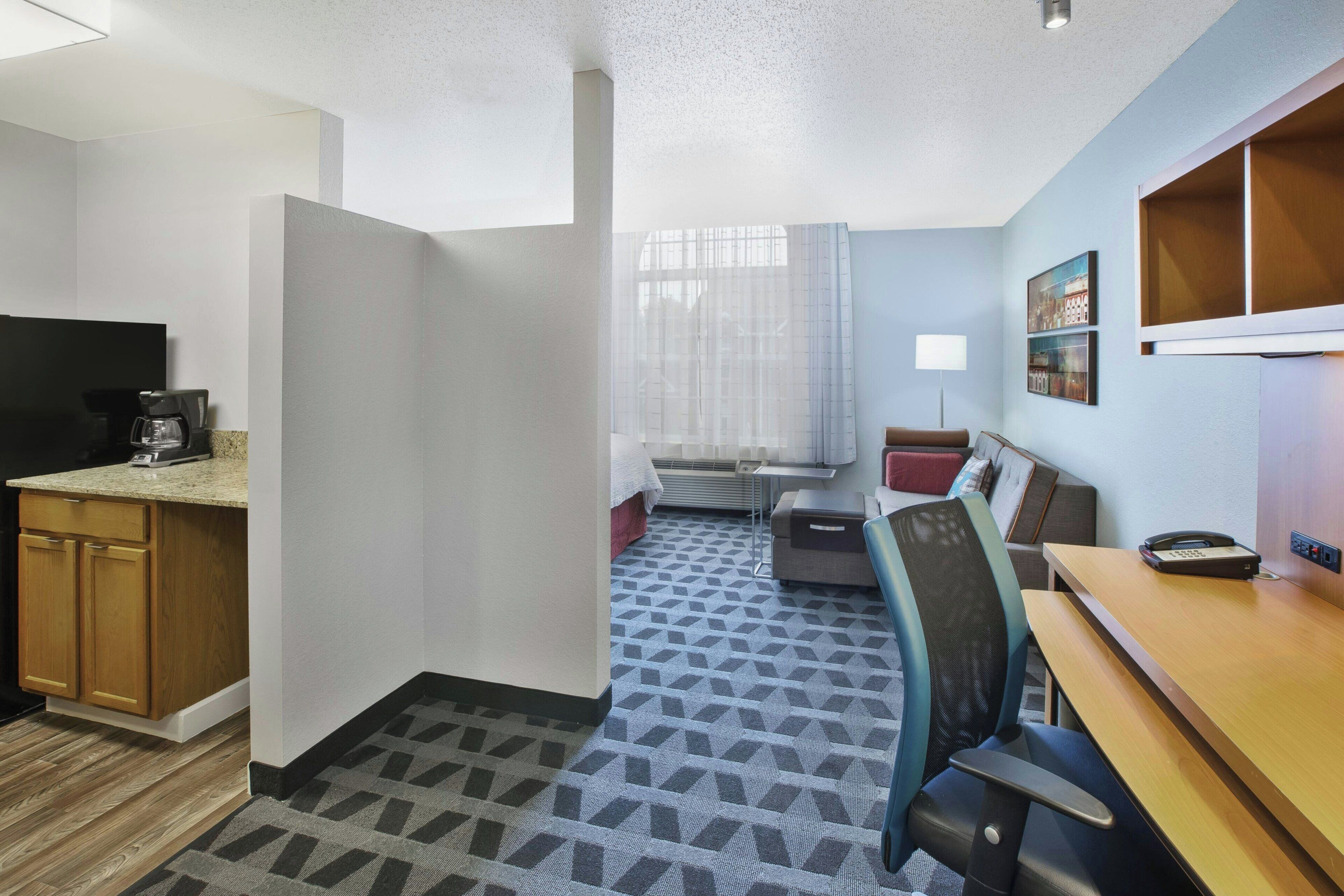 A compact hotel room with a kitchenette, a bed, a desk, and a chair.