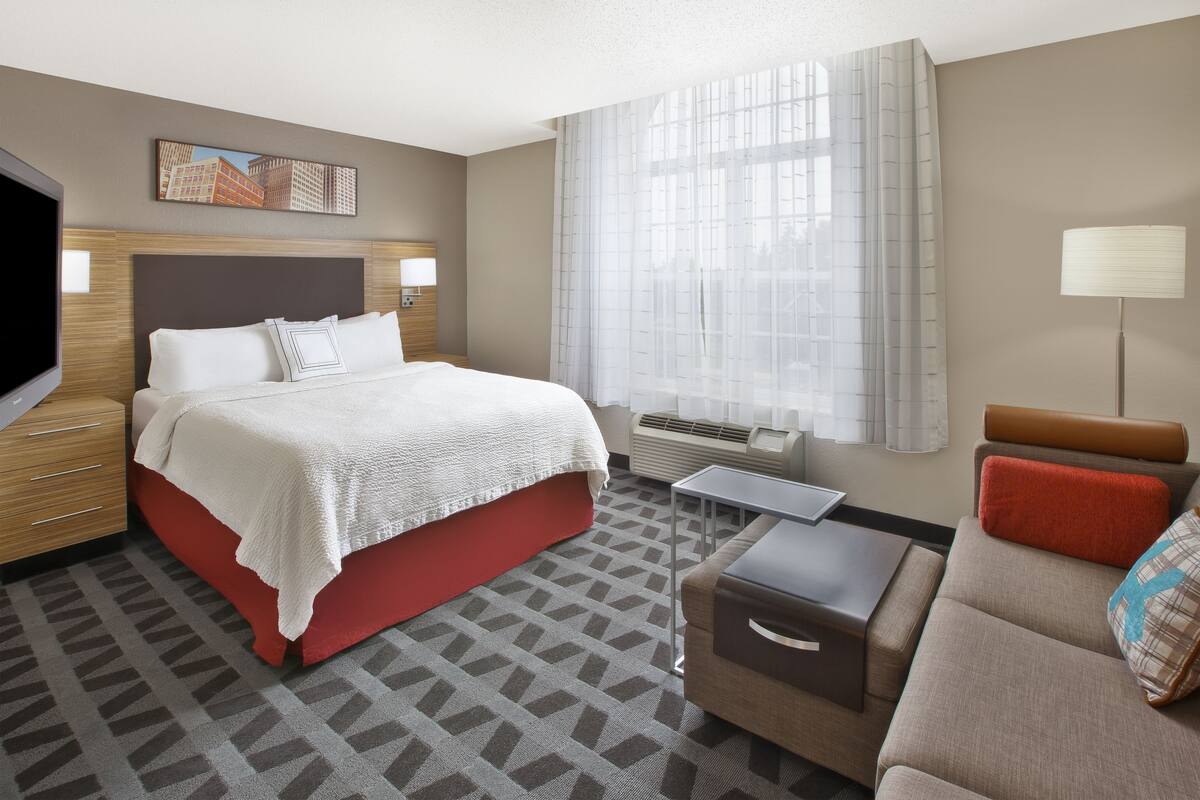 A hotel room with a large bed, a sofa, a desk, and a TV.