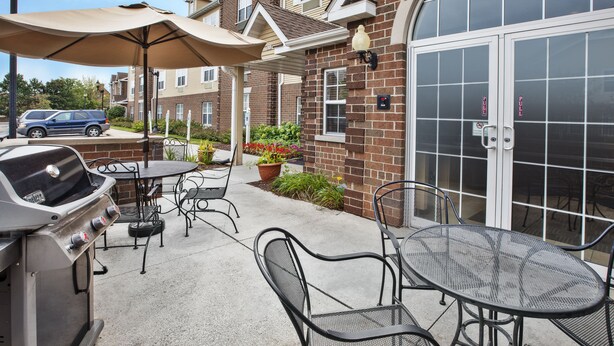 Un patio al aire libre con una parrilla, mesas, sillas y sombrillas.