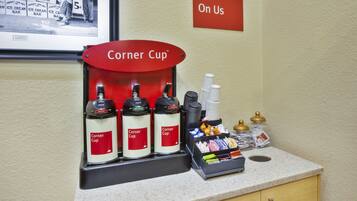 Una estación de bebidas con tres dispensadores Corner Cup, una pila de vasos desechables y una bandeja con condimentos y servilletas.