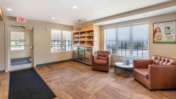 A lobby with a reception desk, a bookshelf, a brown leather sofa, and a large window. - Extended Stay America Suites - Norfolk - Virginia Beach (Virginia Beach)