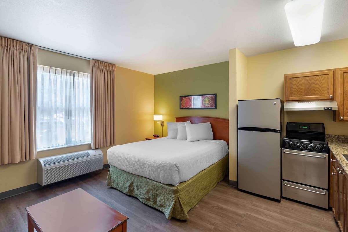 A hotel room with a bed, a refrigerator, a stove, a heater, a nightstand, and a window with curtains.
