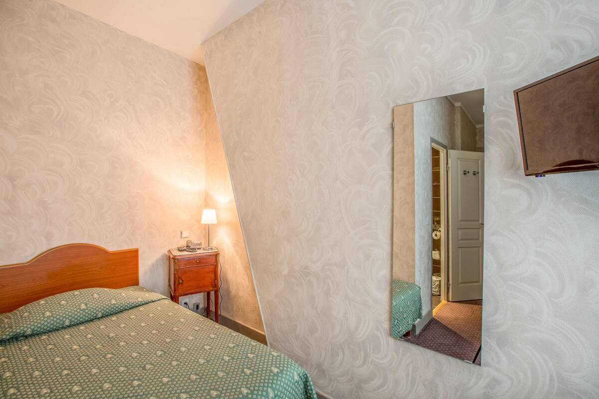 Un dormitorio con cama, mesita de noche, lámpara y un espejo en la pared.
