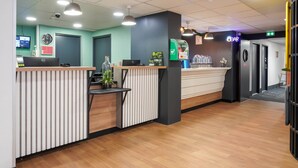 Uma área de recepção com um balcão de madeira, um computador, um relógio e um letreiro de bar.