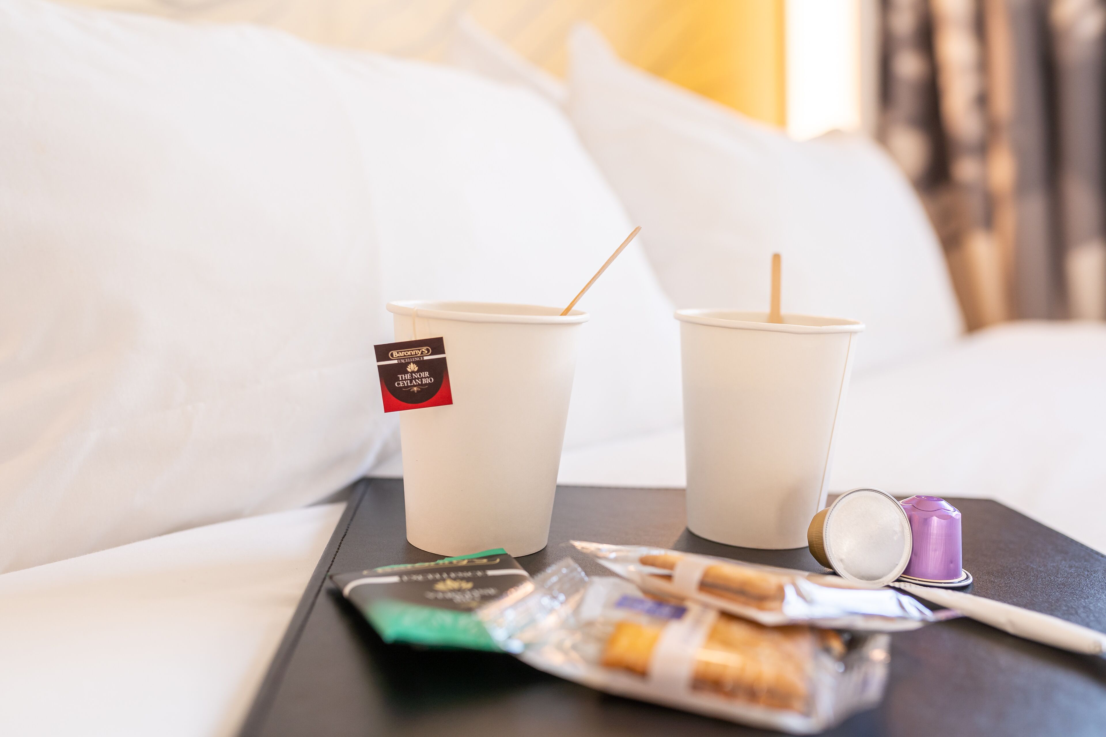 Dos vasos desechables con pajitas sobre una bandeja, un paquete de cigarrillos y un recipiente morado.