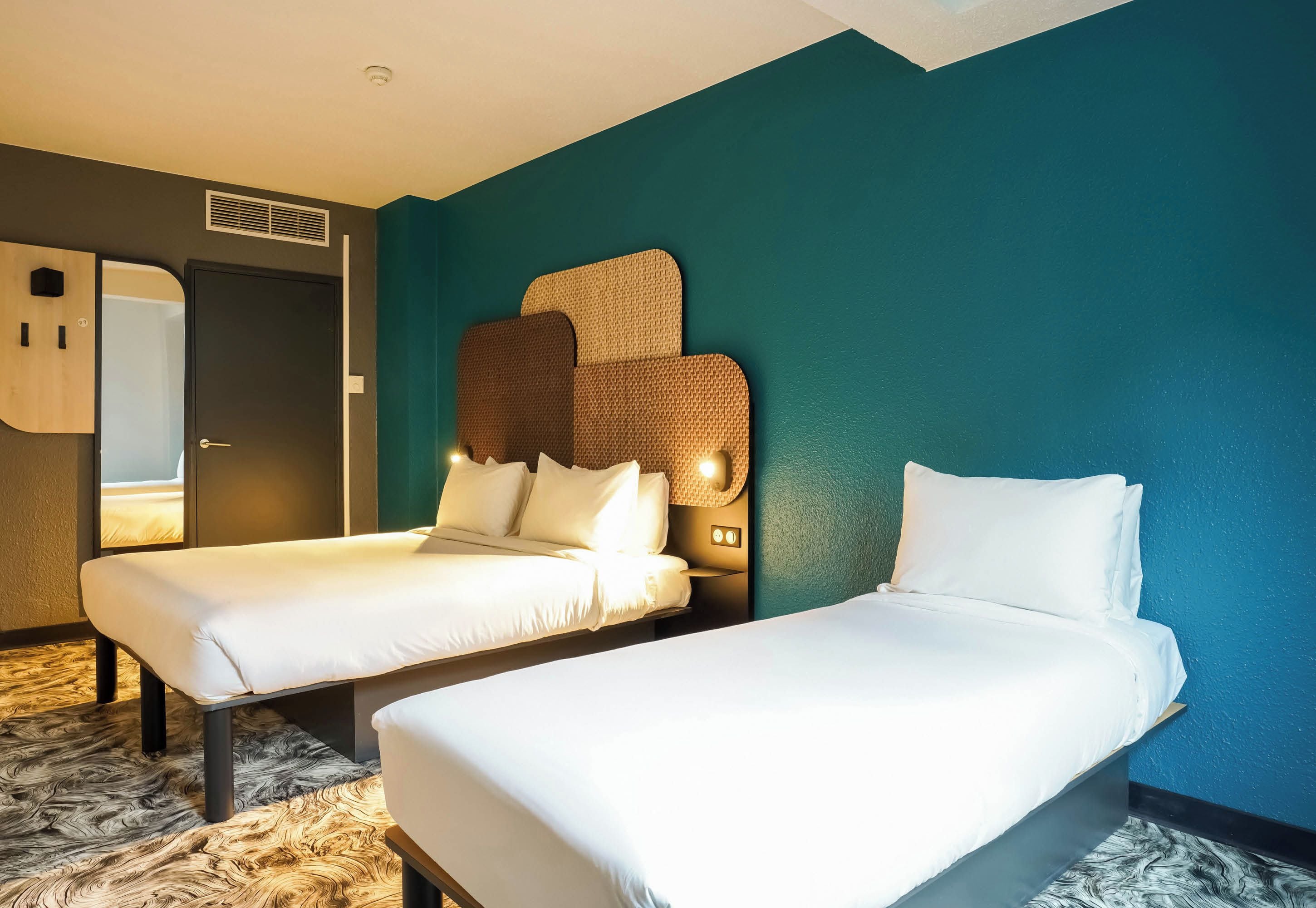 Una habitación de hotel con dos camas individuales, un espejo grande y una pared con textura.