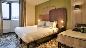 Quarto de hotel com uma cama grande, uma escrivaninha com cafeteira e vista para a cidade pela janela.