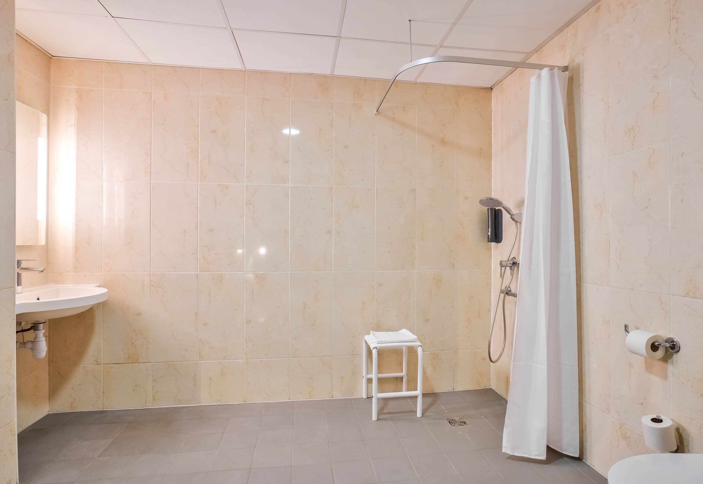 A bathroom with a sink, toilet, shower, and a small stool.