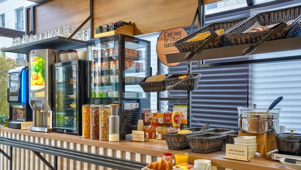 Um buffet de café da manhã com diversos alimentos, uma máquina de café e uma placa indicando ser um café da manhã preparado pelo chef.