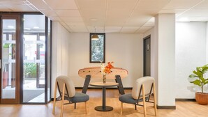 Quarto moderno com uma mesa redonda, duas cadeiras, um vaso de planta e uma janela com vista.