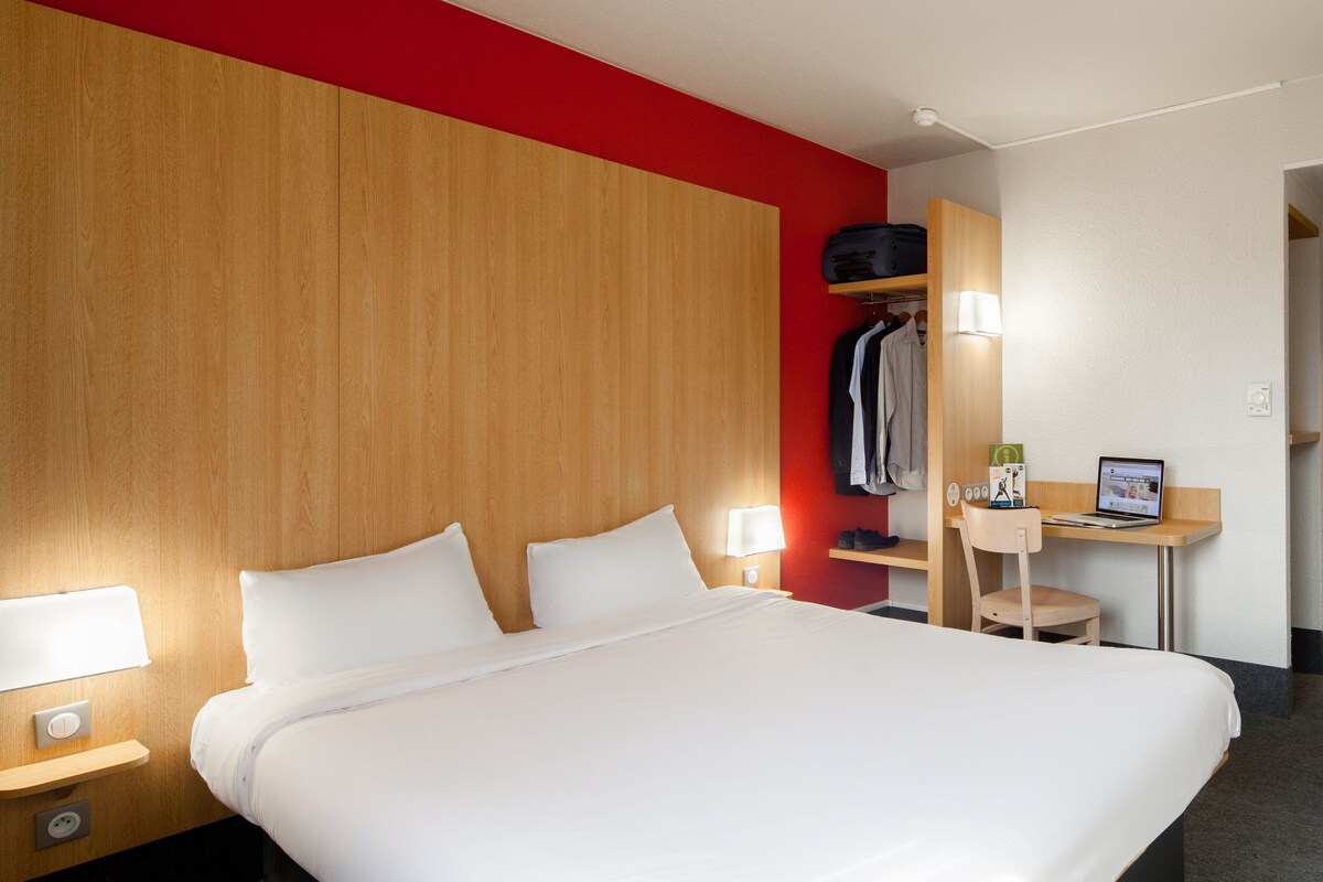 Una habitación de hotel con una cama grande, lámparas de noche, un escritorio con una computadora portátil y un armario.