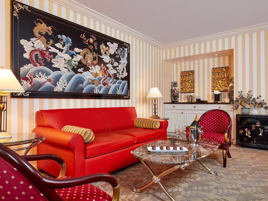 A room with a red sofa, a glass coffee table, striped wallpaper, and a large dragon painting.