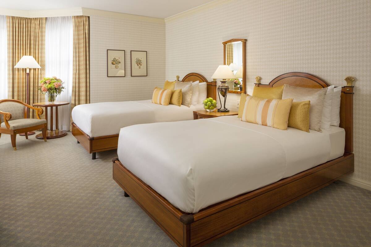 A hotel room with two beds, a sitting area with a chair, a small table, and a lamp.