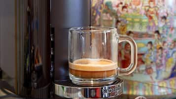 A coffee machine with a glass mug of coffee, a decorative ceramic pot, and chocolate eggs on a glass shelf.