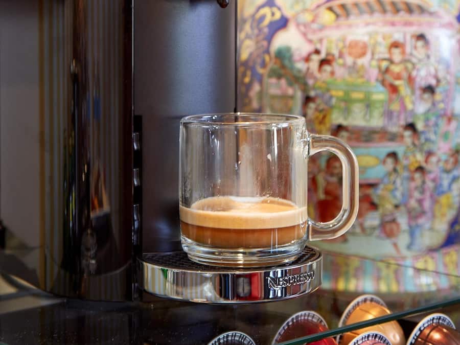 A coffee machine with a glass mug of coffee, a decorative ceramic pot, and chocolate eggs on a glass shelf.