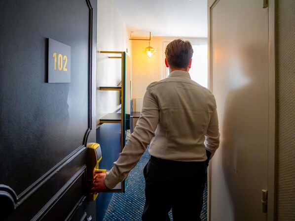 A person entering a room with a number '102' on the wall, a modern door, and a hallway with a patterned floor.