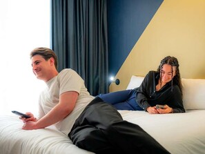 Two people lying on a bed with a smartphone, a window with curtains, and a partial view of a room's wall. - ibis Styles Paris 15 Lecourbe (Paris)