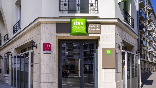 Entrada de un hotel con puerta de cristal, un letrero que dice 'Ibis Styles Hotels' y una señal que indica 'Paris 15 Le Courbe'.