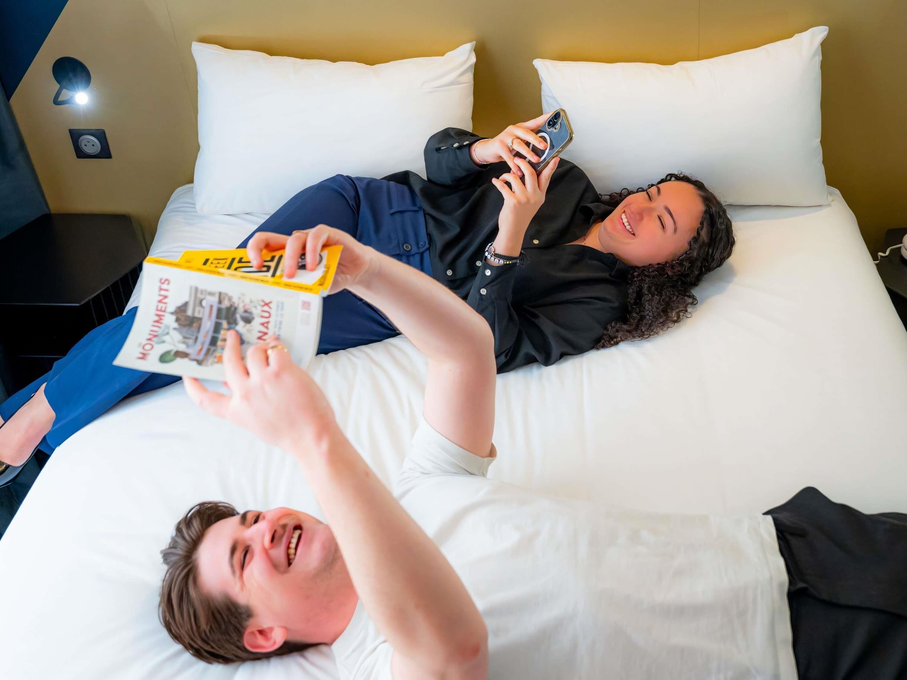 A hotel room with a bed, pillows, a nightstand, and a wall socket.