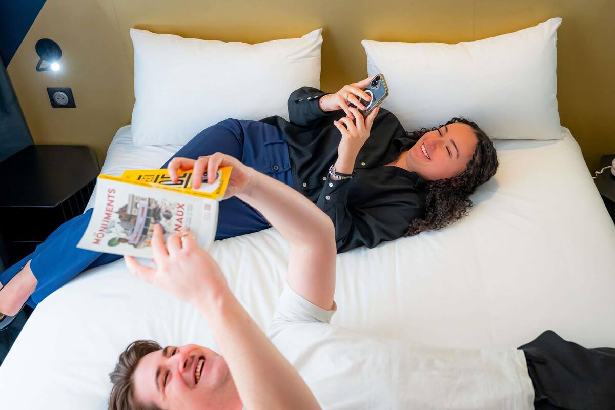A hotel room with a bed, pillows, a nightstand, and a wall socket.