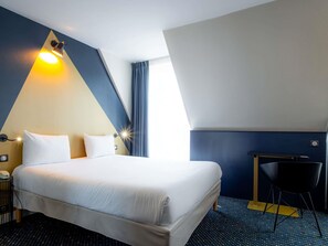 Ein Hotelzimmer mit Bett, Schreibtisch, Stuhl, Nachttisch und Lampe.
