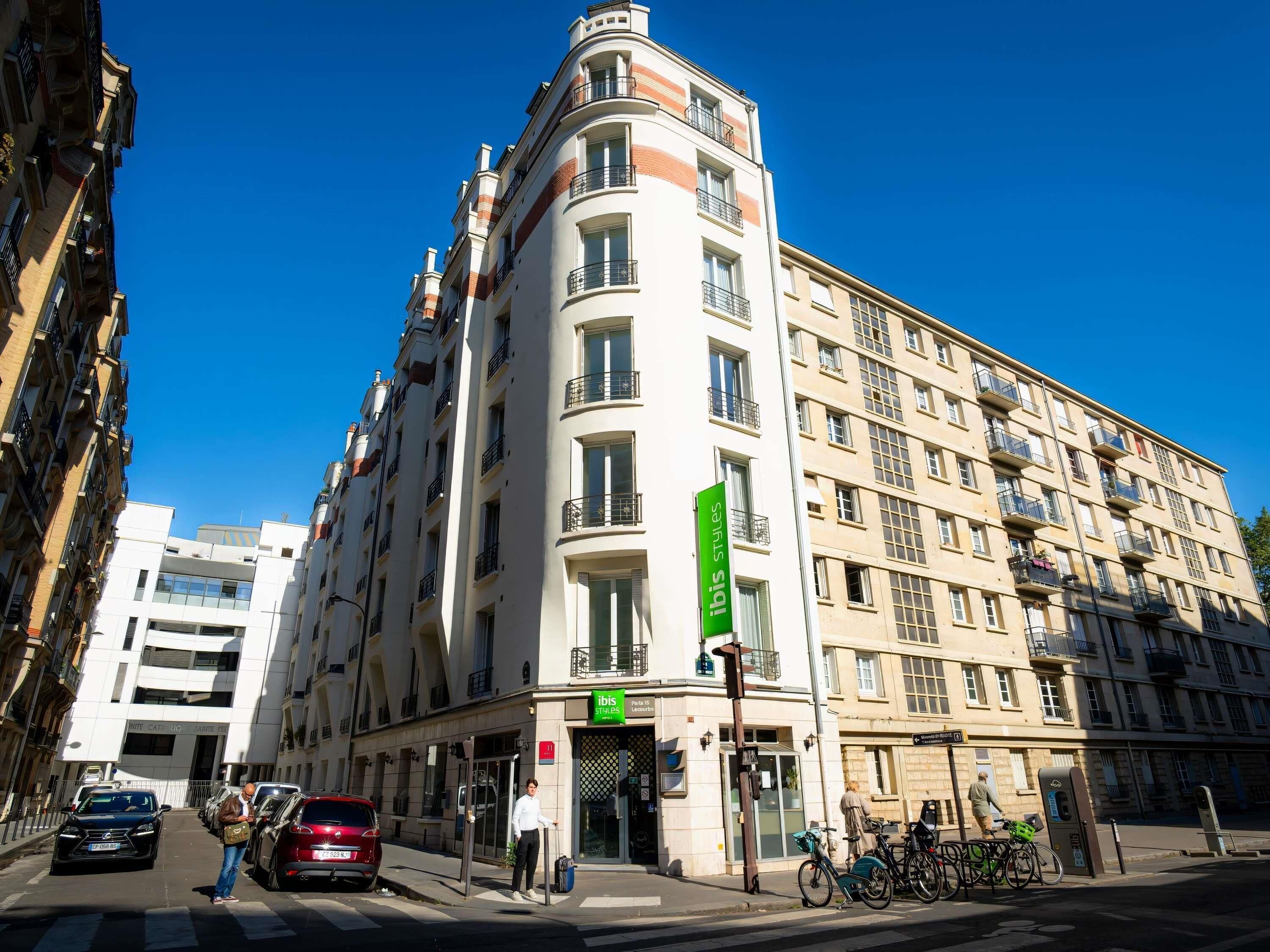 A multi-story building with a prominent green sign, a gated entrance, and parked cars.