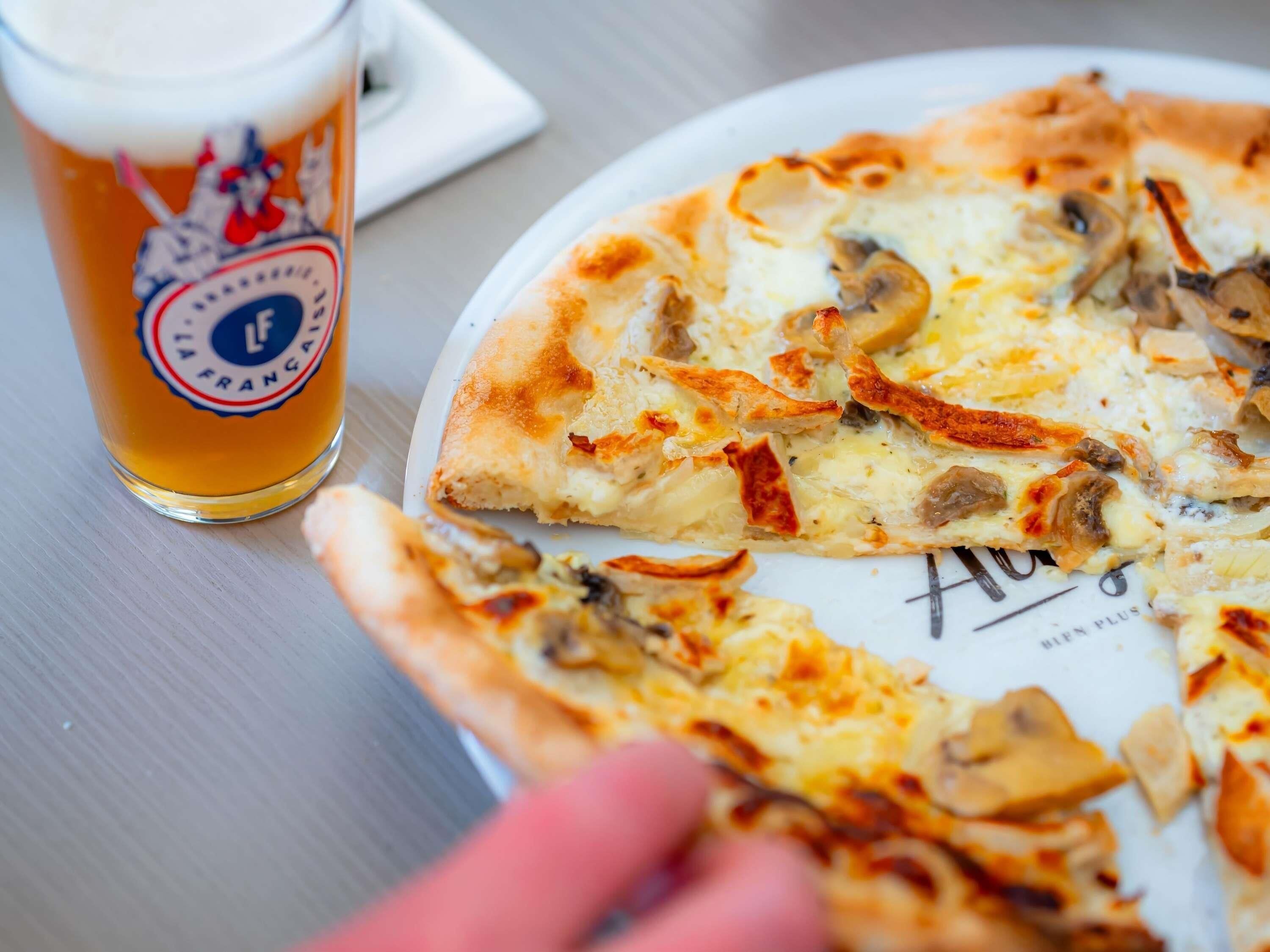 Une pizza dont on a coupé une part, un verre de bière et une main.