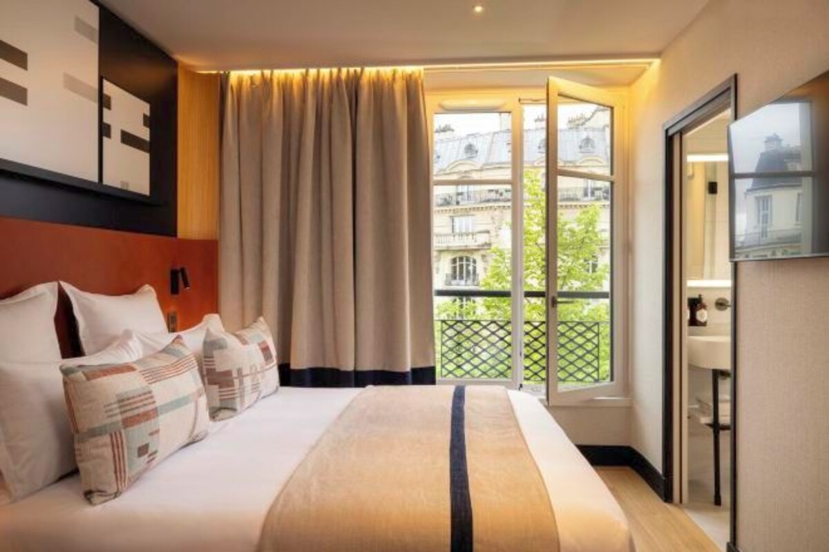 Habitación de hotel con una cama grande, vistas de la ciudad desde un balcón y una decoración de diseño moderno.