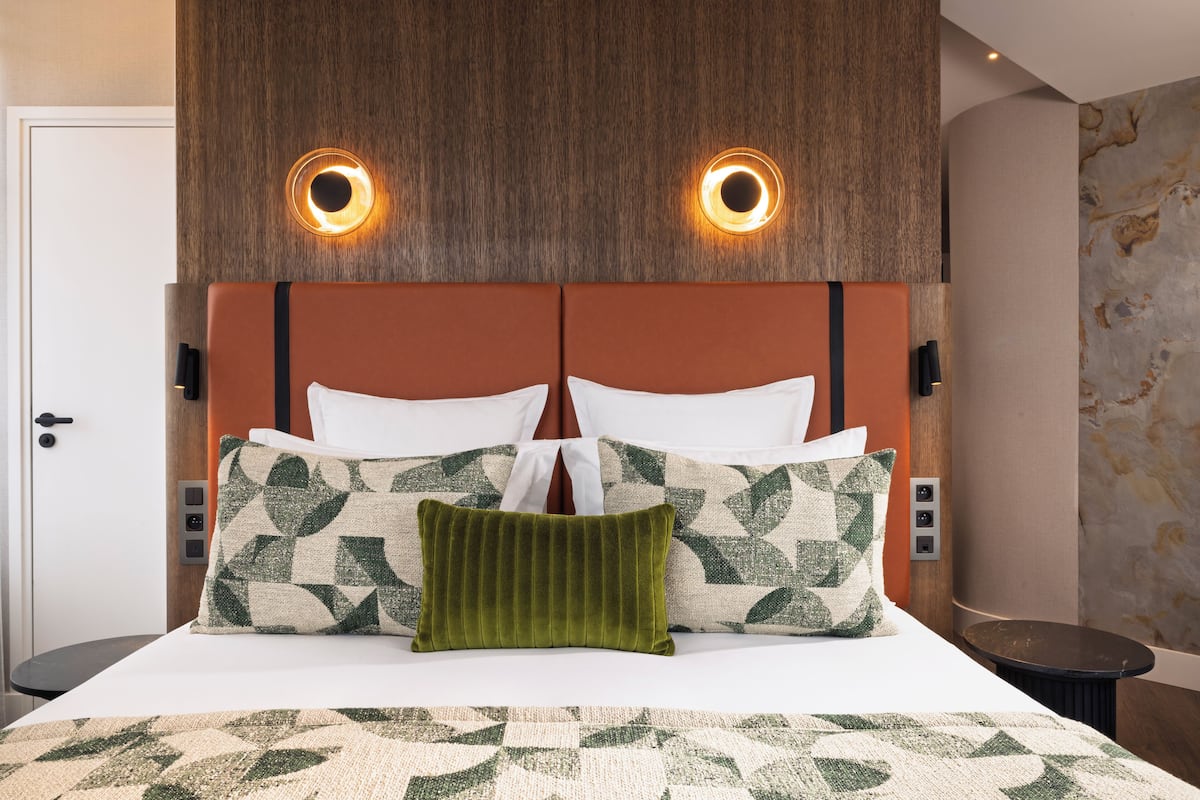 A hotel room with a bed, two wall-mounted light fixtures, a door, and a small round table.